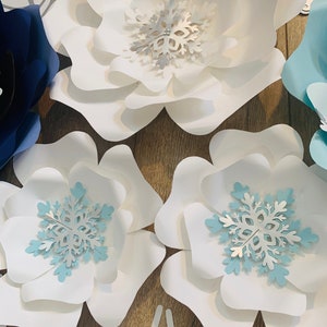 May include: White and blue paper flowers with snowflake embellishments. The flowers are layered and have a delicate, whimsical look.