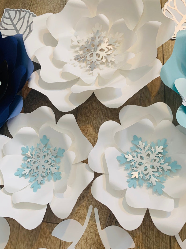 May include: White and blue paper flowers with snowflake embellishments. The flowers are layered and have a delicate, whimsical look.