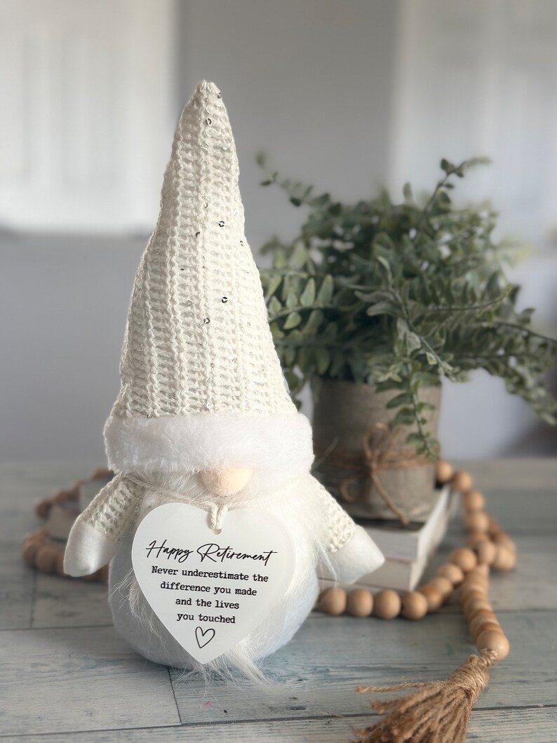 May include: White gnome figurine with a heart-shaped sign that reads "Happy Retirement Never underestimate the difference you made and the lives you touched".
