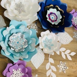 May include: A set of paper flowers in various colors, including white, blue, purple, and black. The flowers are decorated with snowflake cutouts and are arranged on a wooden surface.