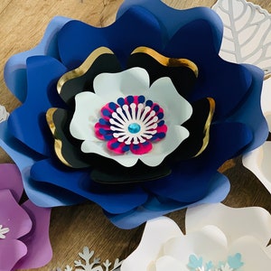 May include: A set of paper flowers in various shades of blue, purple, and white. The flowers are layered and have a 3D effect. The center of the blue flower has a pink and blue design with a sparkly blue jewel.