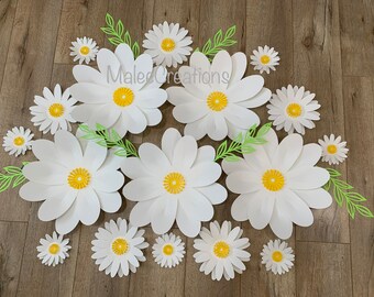 May include: A collection of white paper daisies of various sizes, with yellow centers, arranged on a wood floor. The daisies are layered to create a 3D effect. The text "Male Creations" is visible in the center of the image.