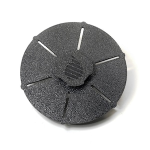 Puede incluir: Disco de lija de plástico negro con una superficie texturizada y seis ranuras alrededor del borde. El centro del disco tiene un área elevada texturizada con un diseño estilizado.