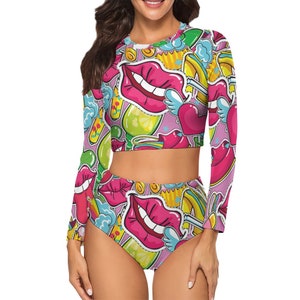 May include: A pink and white two-piece swimsuit with a long-sleeved crop top and high-waisted bottoms. The swimsuit features a colorful, graphic print of lips, hearts, and other playful designs.