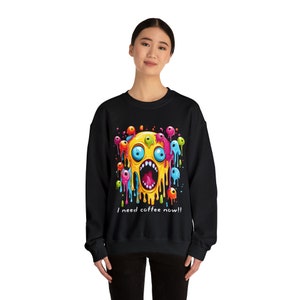 May include: Black sweatshirt featuring a colourful graphic of a screaming face with multiple eyes and the text "I need coffee now!"