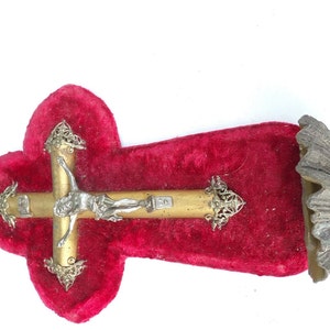 Könnte beinhalten: Ein goldfarbenes Kruzifix mit einer silberfarbenen Jesus Christus-Figur auf einem roten Samt-Hintergrund. Das Kruzifix ist an einer Wand mit einer dekorativen Metallhalterung befestigt.