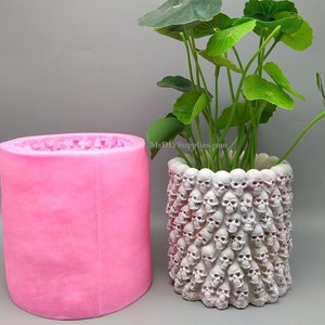 Puede incluir: Molde de silicona rosa para hacer una maceta de calavera. El molde es cilíndrico y tiene una superficie lisa. El molde se muestra junto a una maceta terminada hecha con el molde. La maceta es blanca y tiene un diseño de calavera.