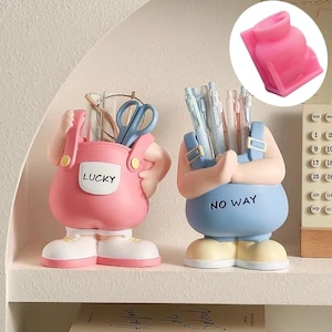 Op de afbeelding: Twee bureau-organizers in de vorm van cartoonfiguren. Eén is roze met het woord "LUCKY" op de voorkant en de andere is blauw met de woorden "NO WAY" op de voorkant.