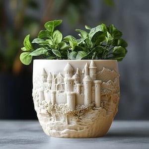 May include: Cream-coloured ceramic plant pot with a detailed relief of a castle scene. The pot features multiple towers, turrets, and architectural details. A green leafy plant grows inside. The pot is a decorative item for home decor.