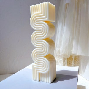 May include: A white ceramic sculpture with a wavy, abstract design. The sculpture is made of stacked, layered pieces that create a three-dimensional effect.