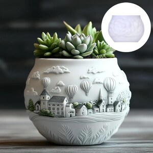 Könnte beinhalten: Weißer Keramik-Blumentopf mit detailliertem Reliefdesign eines Dorfes mit Heißluftballons und Wolken. Der Topf ist mit grünen Sukkulenten gefüllt. Ein charmanter Zusatz für jede Wohnkultur.