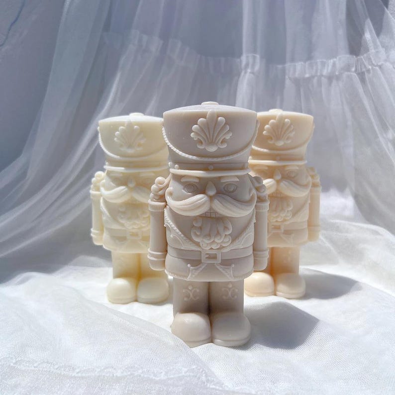 Może przedstawiać: Trzy białe ceramiczne figurki  łamacza orzech&oacute;w. Każda figurka ma na sobie czapkę z pi&oacute;rem i ma wąsy i brodę. Figurki stoją na białym tle.