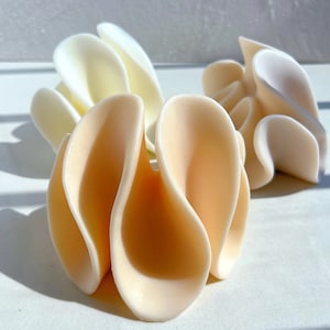 May include: Three ceramic sculptures in the shape of flowers. The sculptures are made of white and peach coloured ceramic and have a wavy, organic shape.