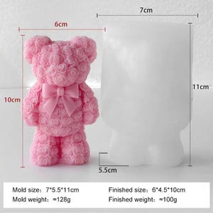 May include: A pink teddy bear candle with a bow, next to a white mold. The finished candle is approximately 10 cm tall and the mold is 11 cm tall. The mold is 7 cm wide and the finished candle is 6 cm wide.