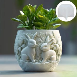 Könnte beinhalten: Weißer Keramik-Pflanztopf in Form eines Kaninchens mit zwei auf der Vorderseite geformten Kaninchen. Der Topf ist mit grünen Blattpflanzen gefüllt.