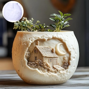 Puede incluir: Jardinera esférica de color crema con un relieve detallado de una casa, una luna y follaje. La jardinera contiene plantas verdes. El exterior tiene una superficie texturizada, similar a un cráter. Un pequeño recipiente redondo de material blanco está en la esquina superior izquierda.