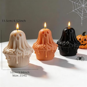 Può includere: Tre candele a forma di cupcake fantasma nei colori beige, arancione e nero, ognuna con uno stoppino acceso. Le candele misurano 11,5 cm di altezza, 10 cm di larghezza e contengono 354 g di cera. Sono visibili anche un ragno e una zucca.