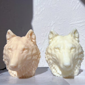 May include: Two white wolf head sculptures, one with a slightly more beige tone than the other. Both sculptures have detailed fur and facial features.
