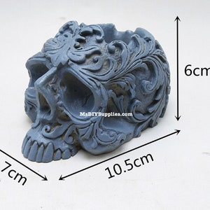 May include: A gray skull-shaped decorative container with ornate floral carvings. The container measures 4.1 inches long, 2.8 inches wide, and 2.4 inches high. The container has a hollowed-out top.