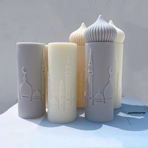 May include: Four decorative candles with a mosque design. Two candles are gray and two are cream colored. The candles are all cylindrical and have a dome-shaped top.
