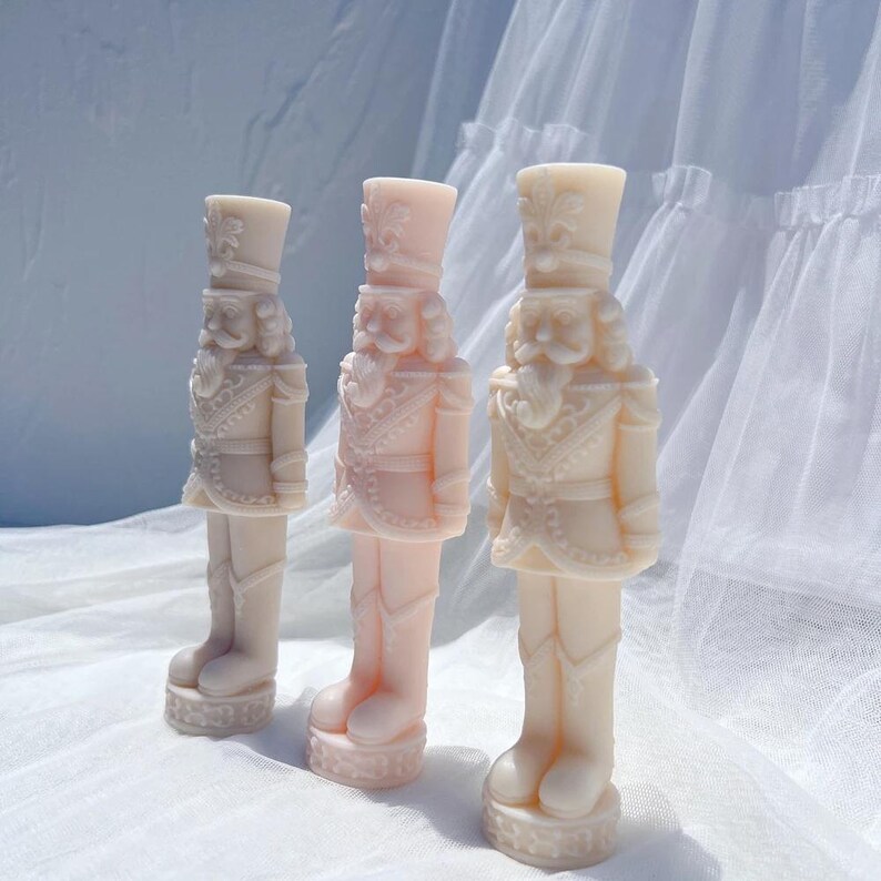 May include: Three pink nutcracker figurines with intricate details and a white background.