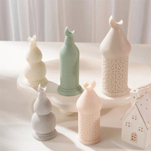 May include: A collection of decorative ceramic lanterns in various shapes and colors. The lanterns include a light green, a pale pink, and a white lantern with a crescent moon design on top. Some lanterns have intricate cut-out patterns.