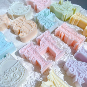 Peut inclure: Une collection de lettres décoratives de couleur pastel avec des motifs complexes. Les lettres sont faites d'un matériau lisse et blanc et sont disposées dans un ordre aléatoire.
