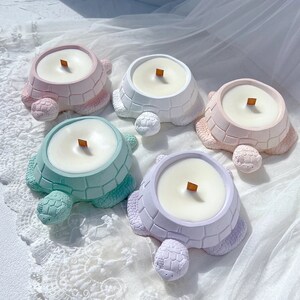 May include: Five turtle-shaped candles in different pastel colours. Each candle has a wooden wick and is made of soy wax.