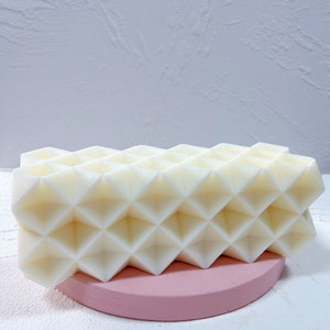 May include: A white geometric soap bar with a honeycomb-like design, resting on a pink circular stand.