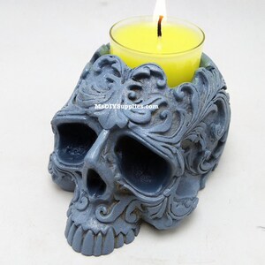 May include: A gray skull-shaped candle holder with intricate floral carvings. A yellow candle burns inside a glass votive. The candle holder has a matte finish and the text "MsDIYSupplies.com" is visible.