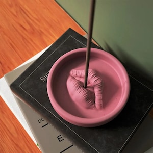 Peut inclure: Porte-encens en céramique rose en forme de lèvres avec un trou au centre pour un bâton d'encens. Le bâton d'encens est dans le trou et brûle.