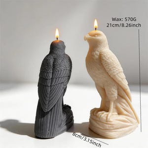 Può includere: Due candele a forma di aquila, una grigio scuro e una color crema, ciascuna con uno stoppino acceso. La candela color crema è alta 21 cm e pesa 570 g. La base della candela color crema misura 8 cm. Entrambe presentano dettagliate texture di piume.