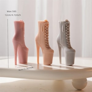 May include: Three high-heeled platform boots in shades of pink and gray are displayed. The boots are 4.72 inches tall and 2.36 inches wide. The boots have a lace-up design and are made of wax. The image includes the text "Wax:58G 12cm/4.72inch 6cm/2.36inch".