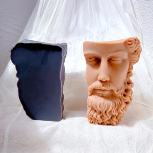 Puede incluir: Un busto de yeso beige de un hombre con barba. El busto está roto en el cuello y la parte superior de la cabeza. El busto está sentado sobre una superficie de tela blanca.