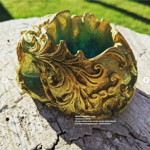 May include: A gold-colored, ornate resin container with a green interior. The container features detailed, swirling patterns and is set on a weathered wooden surface. The text "MaDIYSupplies.com" is visible.