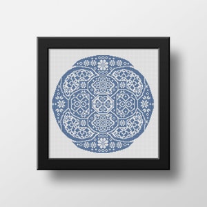 Könnte beinhalten: Ein gerahmtes Kreuzstich-Kunstwerk mit einem kreisförmigen Design in Blau und Weiß. Das detaillierte Muster umfasst florale und geometrische Formen, die eine symmetrische Komposition bilden. Das Kunstwerk wird in einem schwarzen Rahmen präsentiert.