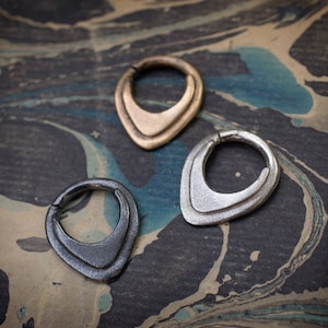 May include: Three silver and gold hoop earrings with a teardrop shape. The earrings are on a marbled surface.
