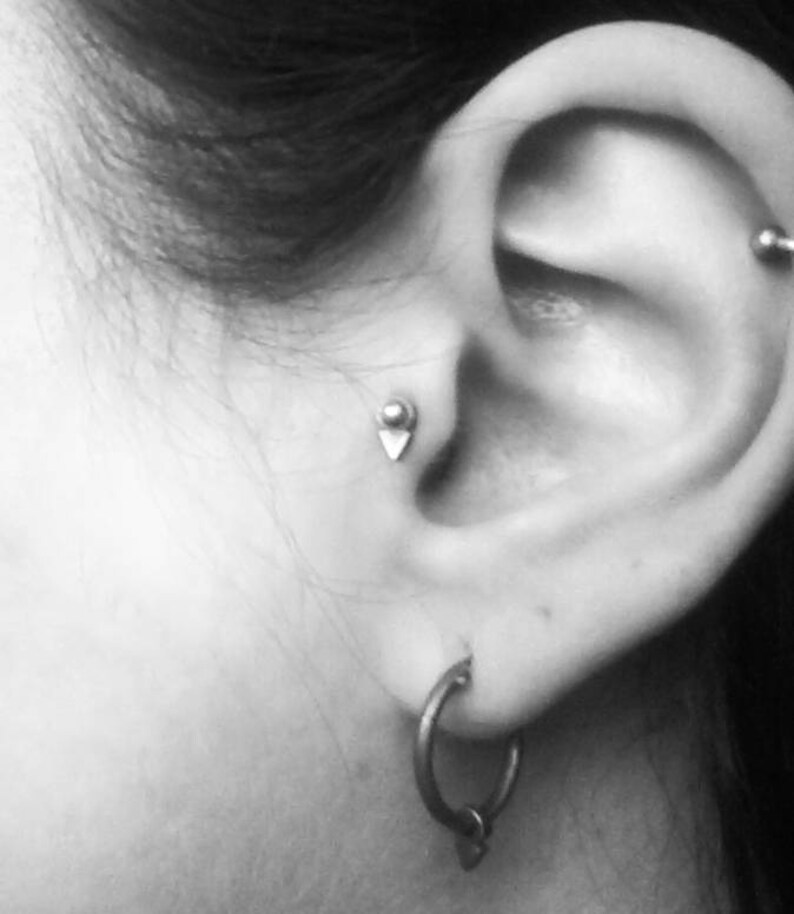 Puede incluir: Primer plano de la oreja de una persona con dos piercings. El piercing inferior tiene un peque&ntilde;o pendiente de plata, y el piercing superior tiene un aro de plata.