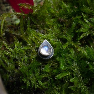 May include: A teardrop-shaped pendant with a silver setting and a round, iridescent moonstone.