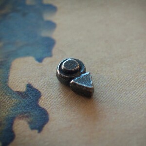 Puede incluir: Una peque&ntilde;a pieza de juego de metal plateado con un c&iacute;rculo y una forma triangular.