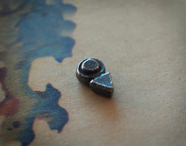 Puede incluir: Una peque&ntilde;a pieza de juego de metal plateado con un c&iacute;rculo y una forma triangular.