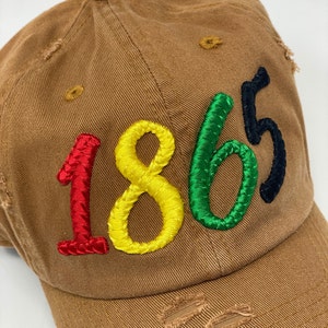 May include: A brown baseball cap with the year 1865 embroidered in red, yellow, green, and black thread.