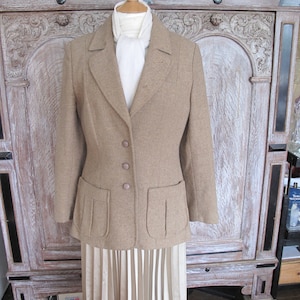May include: A brown tweed jacket with a white scarf and a pleated skirt. The jacket has two large pockets and a button closure.