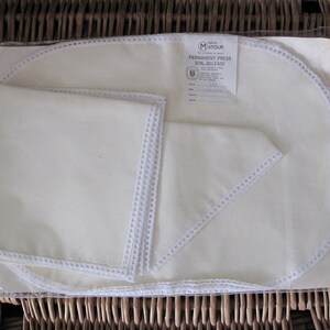 May include: Set of four white linen placemats with white crocheted edging. The placemats are packaged in a clear plastic bag with a label that reads "Matouk Permanent Press Soil Release".