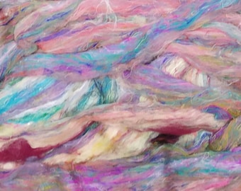 May include: A close-up of a pile of colorful silk threads. The threads are a mix of pink, purple, blue, and cream colors. The silk threads are soft and have a slight sheen. The threads are tightly packed together.