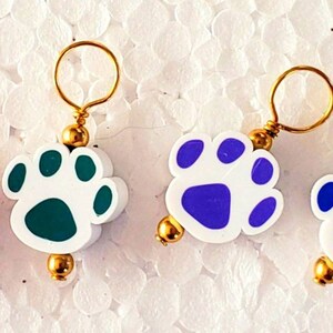 May include: Six colorful paw print stitch markers with gold wire loops. The paw prints are red, yellow, green, purple, blue, and black.