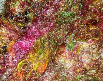 May include: A close-up of a pile of colorful banana silk threads. The threads are a mix of red, yellow, green, and gold.