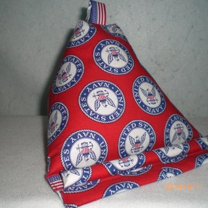 May include: A red triangular pillow with a white and blue pattern of the United States Navy seal. The pillow is made of fabric and has a white and blue striped top.