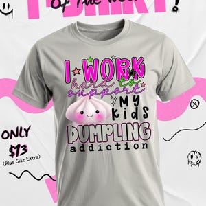 May include: A light gray t-shirt with the text "I work hard to support my kids dumpling addiction" in pink and green. A cartoon dumpling is featured on the shirt. The words "T-SHIRT of the week" are at the top.