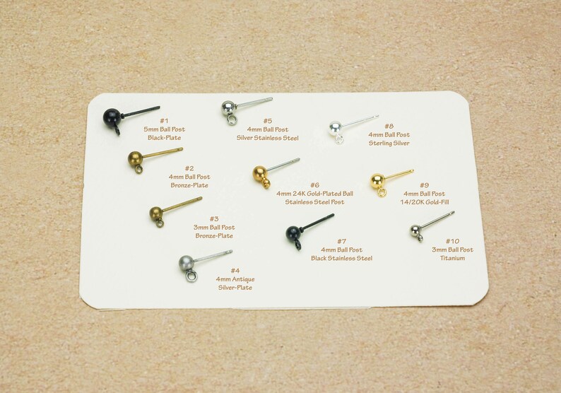 Peut inclure: Diverses tiges de boucles d'oreilles sont pr&eacute;sent&eacute;es sur une carte blanche. Les tiges varient en taille et en couleur, notamment noir, bronze, argent et or. Le texte sur la carte indique la taille et le mat&eacute;riau de chaque tige, comme "5mm Ball Post Black-Plate."